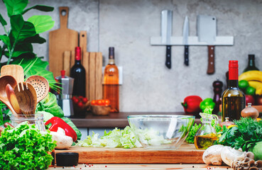 Healthy eating, cooking, food blogging background with empty salad bowl and iceberg lettuce on cutting board, wine bottle, mushrooms and other vegetables and herbs on cozy kitchen with wooden table
