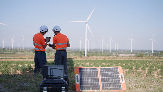 Two Asian inspectors are using a tablet, a clipboard, and solar panel configurations to support renewable energy monitoring and field inspections.