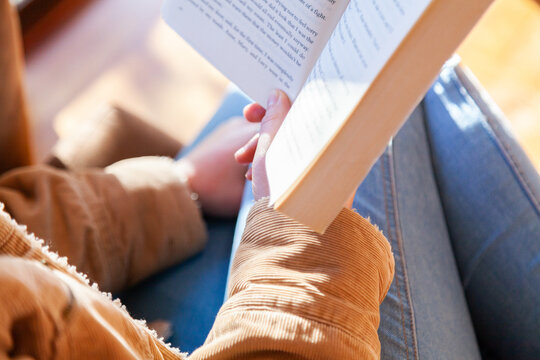 Teen girl reading a novel in the lounge room by a window in winter