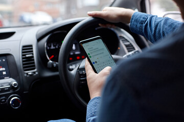 Asian man driving in his car looking down at mobile phone texting