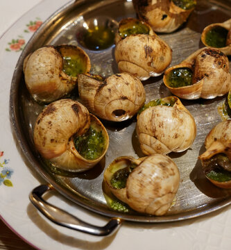Escargots de Bourgogne, served on a metal tray. The snails are cooked in their shells with a green garlic and herb butter sauce.