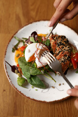 Toasted bread sandwich with guacamole, red fish, egg and greens on a plate on a brown table