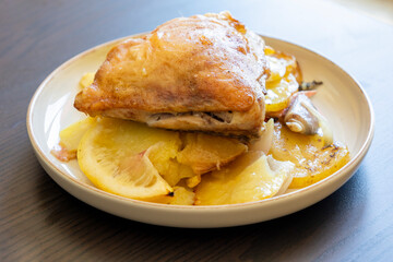 roasted chicken thigh with potatoes, lemons, and shallot onions in a dish close-up