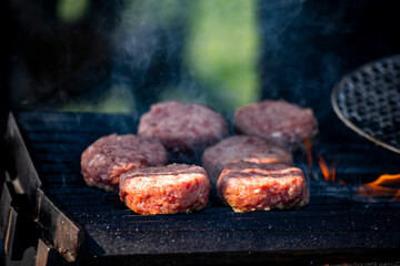 several thick hamburger patties sizzle on the charcoal grill