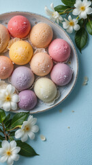 Multi-colored Japanese ice cream Mochi in rice dough and Jasmine flowers on a concrete blue background. Traditional Japanese dessert on a white plate. Top view with copy space. Flat lay 