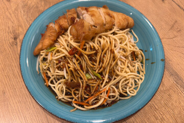 , Deutschland, Rheinland-Pfalz,  27.03.2025,  Frisch gebratene Nudeln mit Gemüse, Sojasauce und knusprigem Hähnchenfilet – serviert auf blauem Teller.