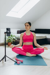 A woman in a pink sports suit conducting an online workout session via her smartphone