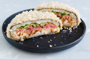 Sushi burger with tuna, cucumber, onion, cheese and rice in nori with crispy crust on a black plate on a gray background. Creative dish. Hybrid food concept. Horizontal orientation. Selective focus.