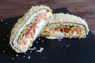 Sushi burger with tuna, cucumber, onion, cheese and rice in nori with crispy crust on a black plate on a wooden table. Creative dish. Hybrid food concept. Horizontal orientation. Selective focus.