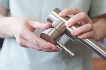 Close-up of hands adjusting a stainless kitchen faucet
