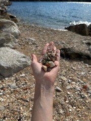 woman's hand holding sea pebbles mixed with glass on the beach near the water. Ecology and pollution of the world ocean