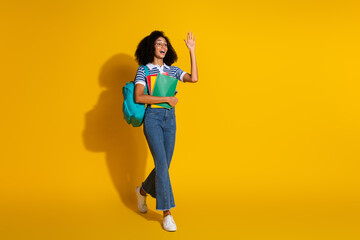 Smiling young woman gesturing hello with a cheerful expression and trendy style against a vibrant yellow background