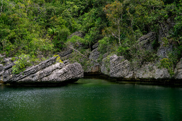 Tropical cliff cove with layered rocks and dense jungle touching emerald green lagoon