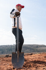 A black iron shovel is firmly stuck in the ground, held by a male worker. The low-angle shot...