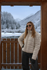 A girl dressed warmly in a white puffer jacket and black pants stands peacefully against a wooden...