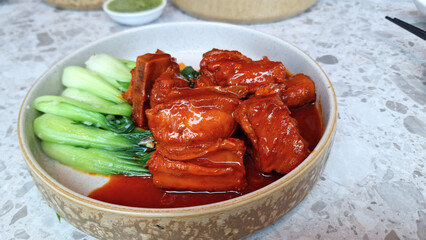 A plate of tender, honey-glazed pork ribs with fresh vegetables rests on a rustic wooden table.