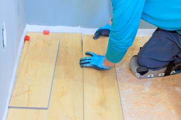 Worker carefully lays down laminate flooring planks in residential room space