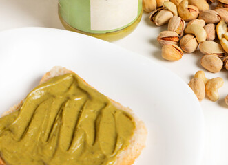tasty pistachio cream on toast isolated on plate or table. woman hand spread the paste with kitchen knife. seeds thrown chaotic on white surface.space for text,advertising banner.