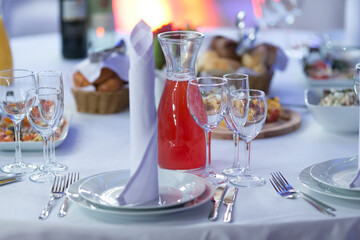 A table is set with plates, wine glasses, and a red liquid pitcher