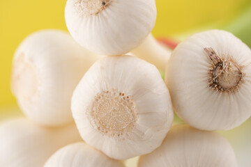 Fresh white garlic bulbs stacked on a bright yellow background showcase their smooth texture and natural beauty
