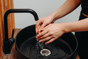 washing hands with clear water close-up, black sink and black tap in cozy bathroom, young caucasian woman, waking in morning, natural beauty, personal hygiene concept