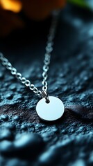 A silver chain necklace with a circular pendant on a rock
