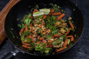 Vegan carrot, broccoli and cauliflower stir fry with nuts and seeds, black wok