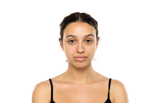 Young woman with natural appearance, no makeup, looking directly at camera. Slight smile, friendly expression. Dark hair in bun. Studio portrait on white background