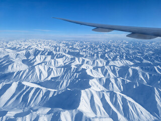View from a flying airplane on snow-capped mountains and an airplane wing. Beautiful winter...