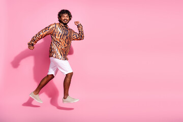 Fashionable young man in patterned shirt jumping joyfully against pink backdrop in casual summer...