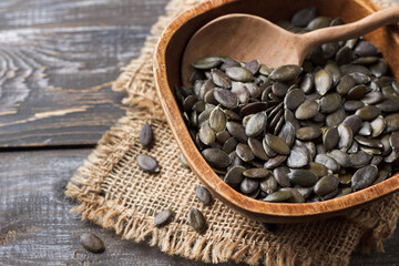 Raw pumpkin seeds in a rustic wooden bowl on wooden table, copy space.