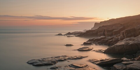 Fototapeta premium Sunset at rocky coastline with serene water and golden sky during twilight
