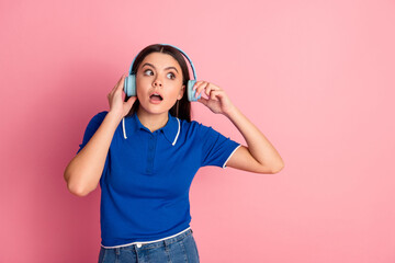 Surprised young woman listening to music on blue headphones against a bright pink background