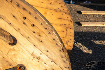 Closeup on a wooden cable drum on the ground.  A smaller, plastic one, close by. Sunlit scene with...