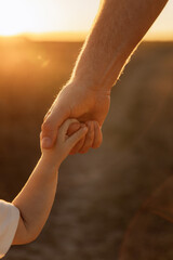 Close-up photo of a child's hand holding his father's hand and leading him on the sunset.  Parental support and development assistance