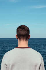 Fototapeta premium Back view of man standing in front of the ocean under blue sky, minimalist lifestyle and nature concept
