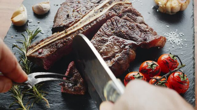 Sliced medium-rare T-bone steak with herbs and garlic on the serving slate board close-up.