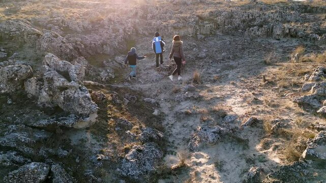 Woman and two kids exploring a rocky landscape on a cloudy day, walking among weathered stone formations in a dry, natural environment