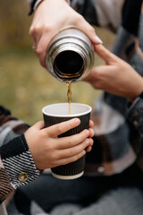 Close-up photo of a mother pouring warm tea into a glass for her son to keep warm