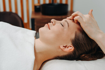 face massage, young attractive caucasian woman, beautiful relaxed lady with closed eyes smiling, white towel, spa therapist doing facial and head massage in beauty salon, skincare and bodycare concept