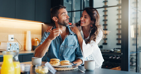 Feeding, happy and couple with breakfast in kitchen for romance on weekend morning together. Love, eating and woman with man for healthy meal for nutrition with fun in marriage in home with helping.