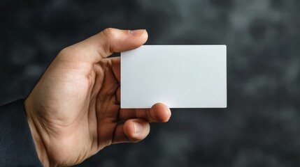 Fototapeta premium A hand holding a blank white business card against a dark blurred background perfect for mockups and presentations