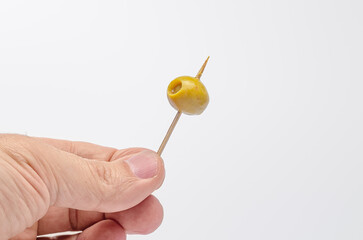 Hand presenting a green olive on a toothpick for a mediterranean appetizer