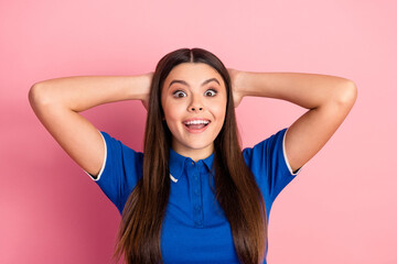 Fototapeta premium Smiling young woman with long brunette hair posing with hands behind head against a pink background.