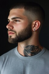 Obraz premium Strong profile of a young man with a well-groomed beard and intricate neck tattoo posing against a dark background during a studio session