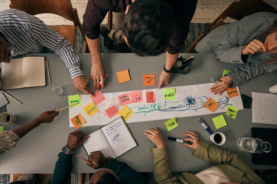 Directly above shot of male and female colleagues discussing business plan over adhesive notes on table in office