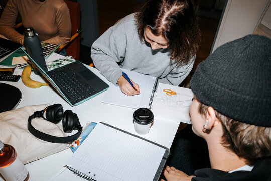High angle view of young woman writing on diary while studying with friends in classroom at university