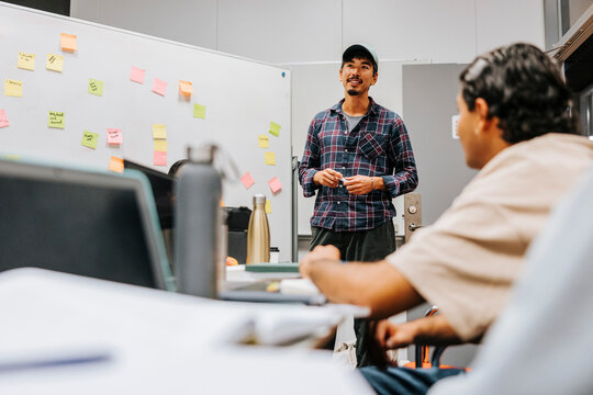 Low angle view of man standing near whiteboard while discussing with friends in project meeting at university classroom