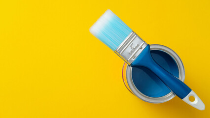 Blue paintbrush resting on an open can of blue paint on a vibrant yellow background. DIY, art, and...