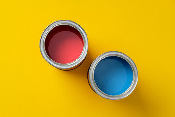 Two open paint cans, one red and one blue, on a vibrant yellow background. DIY, art, and home...